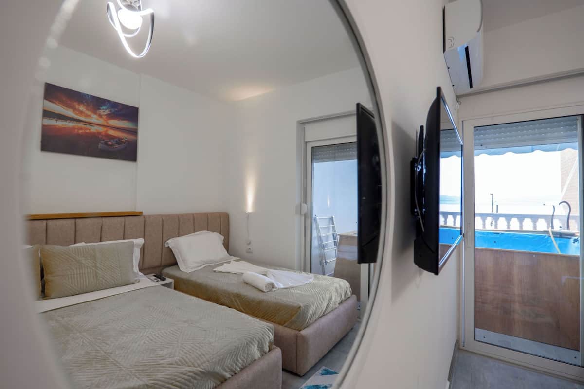 A hotel room with two beds, a TV, a painting, and a balcony with a pool.