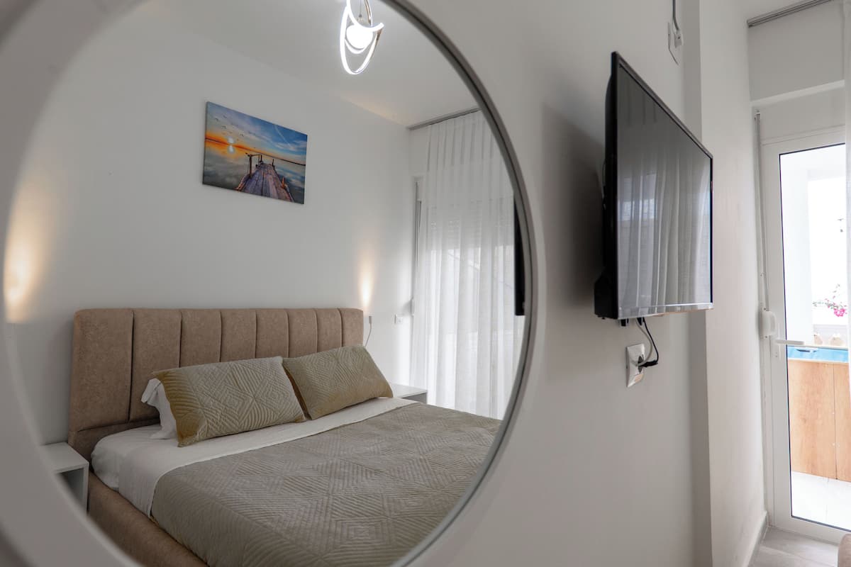 A bedroom with a bed, a TV mounted on the wall, and a painting on the wall.