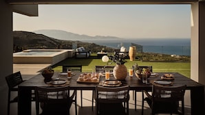Une table à manger dressée pour un repas, avec vue sur la mer et les montagnes.