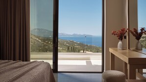 Une chambre dotée d’une grande porte-fenêtre coulissante donnant sur un balcon avec vue sur la mer et les collines.