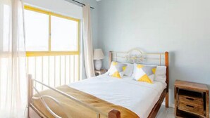Une chambre à coucher avec un lit, une table de chevet, une commode et une fenêtre avec des rideaux.