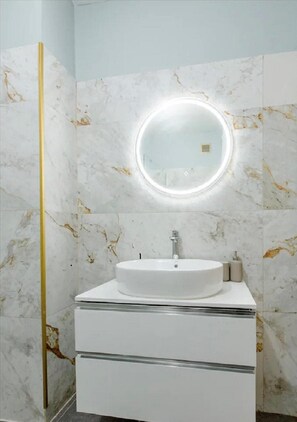 Een badkamer met een wit wastafelmeubel, een ronde spiegel met verlichting, en marmeren wanden.