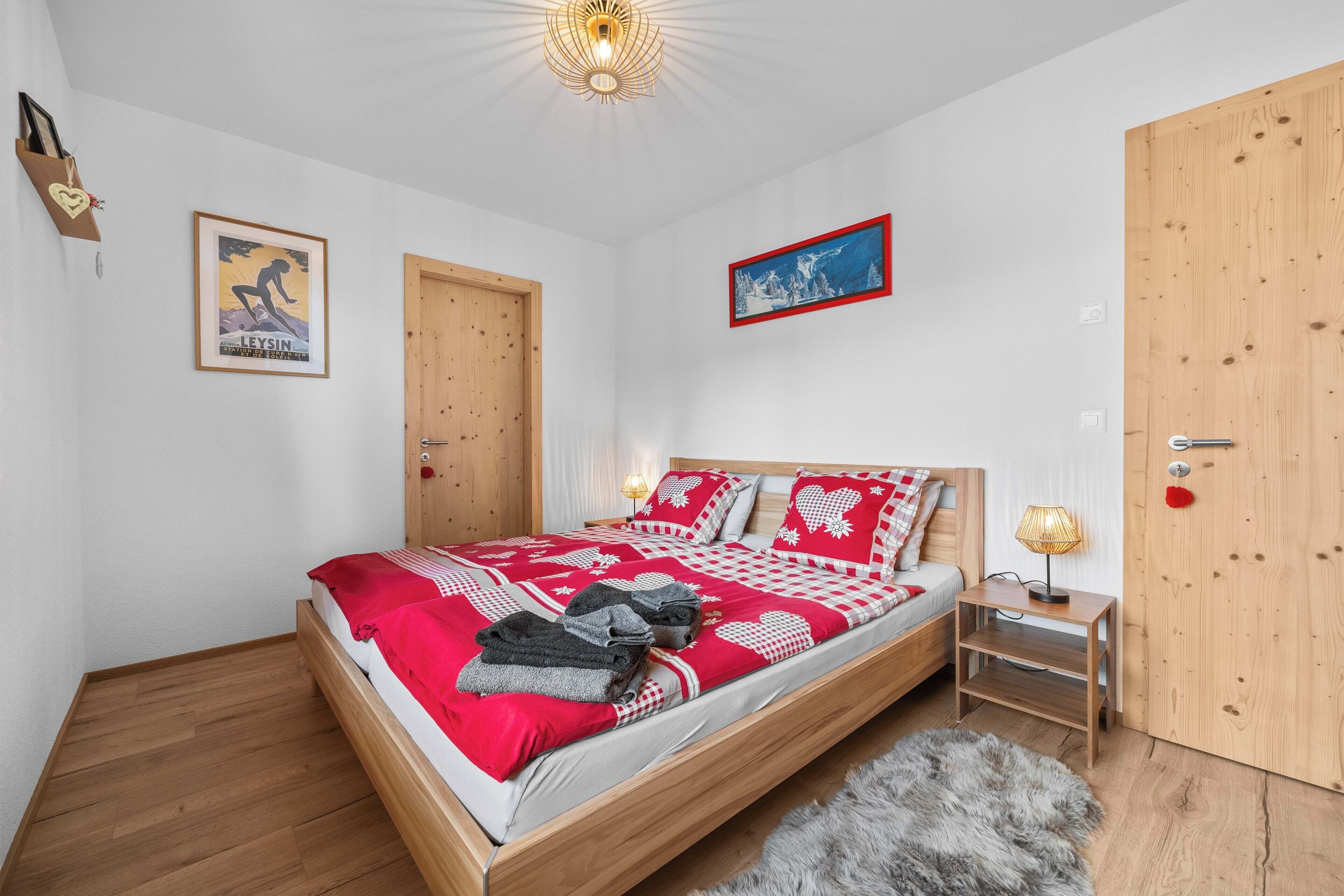 A bedroom with a wooden bed, a red and white checkered bedspread, a fluffy grey rug, and a wooden door.