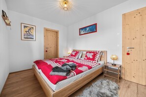 A bedroom with a wooden bed, a red and white checkered bedspread, a fluffy grey rug, and a wooden door.