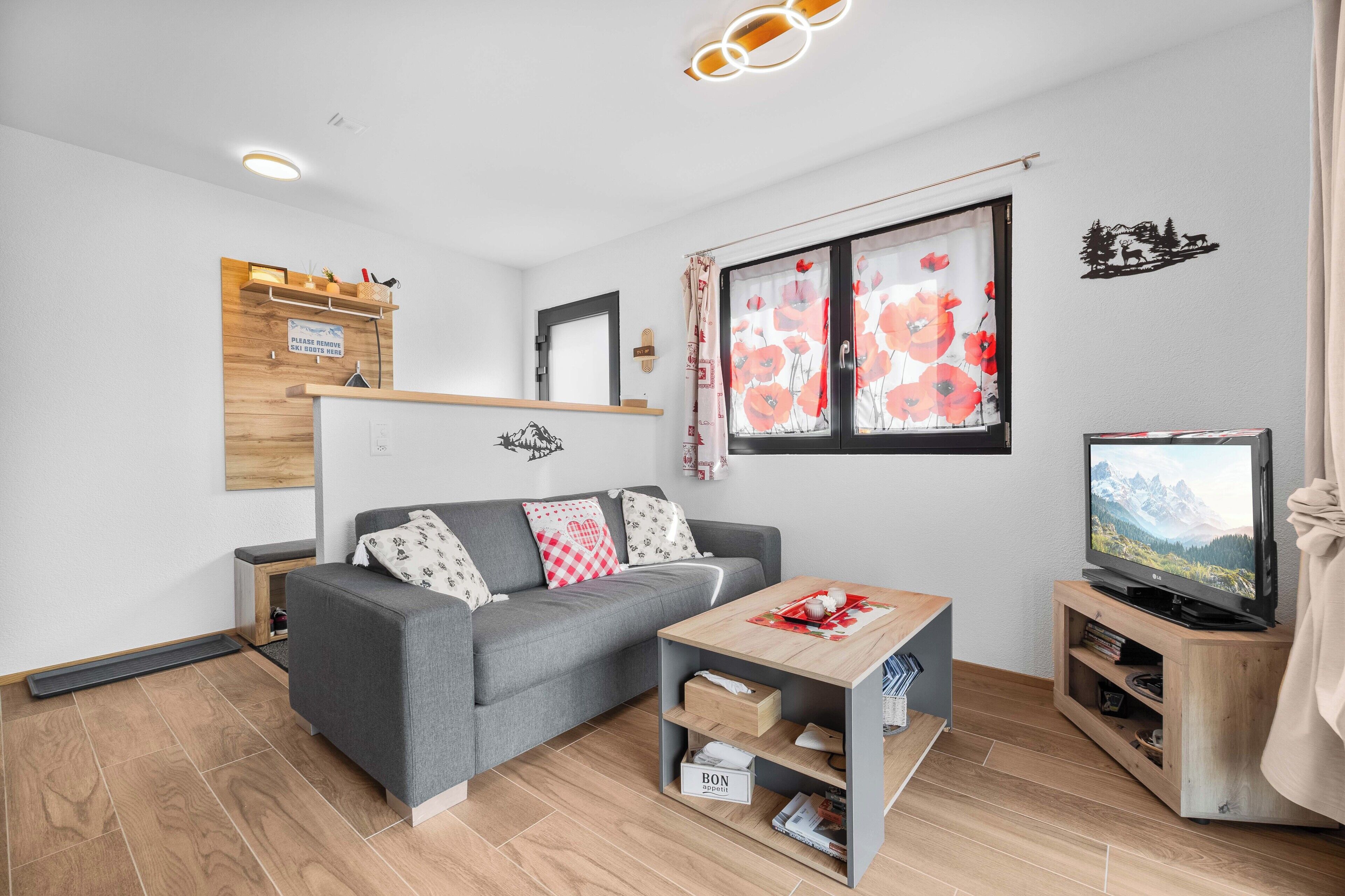 A modern living room with a grey sofa, a wooden coffee table, and a television on a wooden stand.