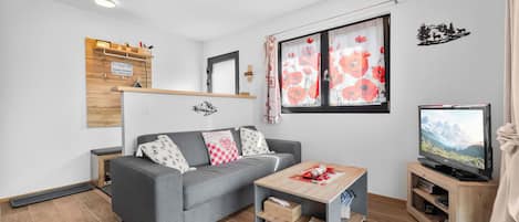 Una sala de estar moderna con un sofá gris, una mesa de centro de madera y un televisor sobre un mueble de madera.