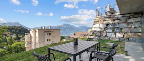 An outdoor patio with a table and chairs, overlooking a mountainous landscape and a residential area.
