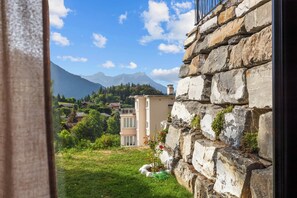 A stone wall with a view of a mountainous landscape and a building with a balcony.