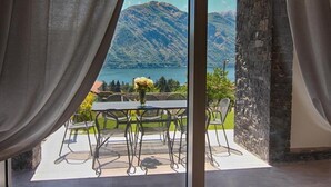 Une terrasse avec une table et des chaises, un vase de fleurs et une vue sur un lac et des montagnes.