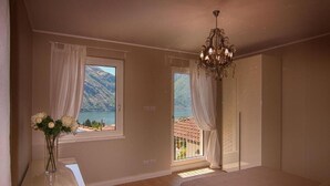 Une chambre à coucher avec un lit, une table de chevet, un vase de fleurs et une vue sur les montagnes et un lac, visible par les fenêtres.