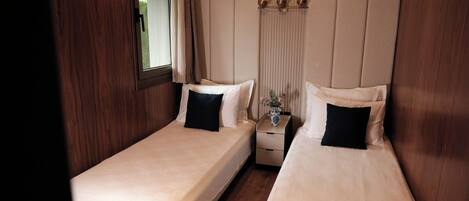 A small, cozy room with two single beds, a nightstand with a vase, and a window with curtains.