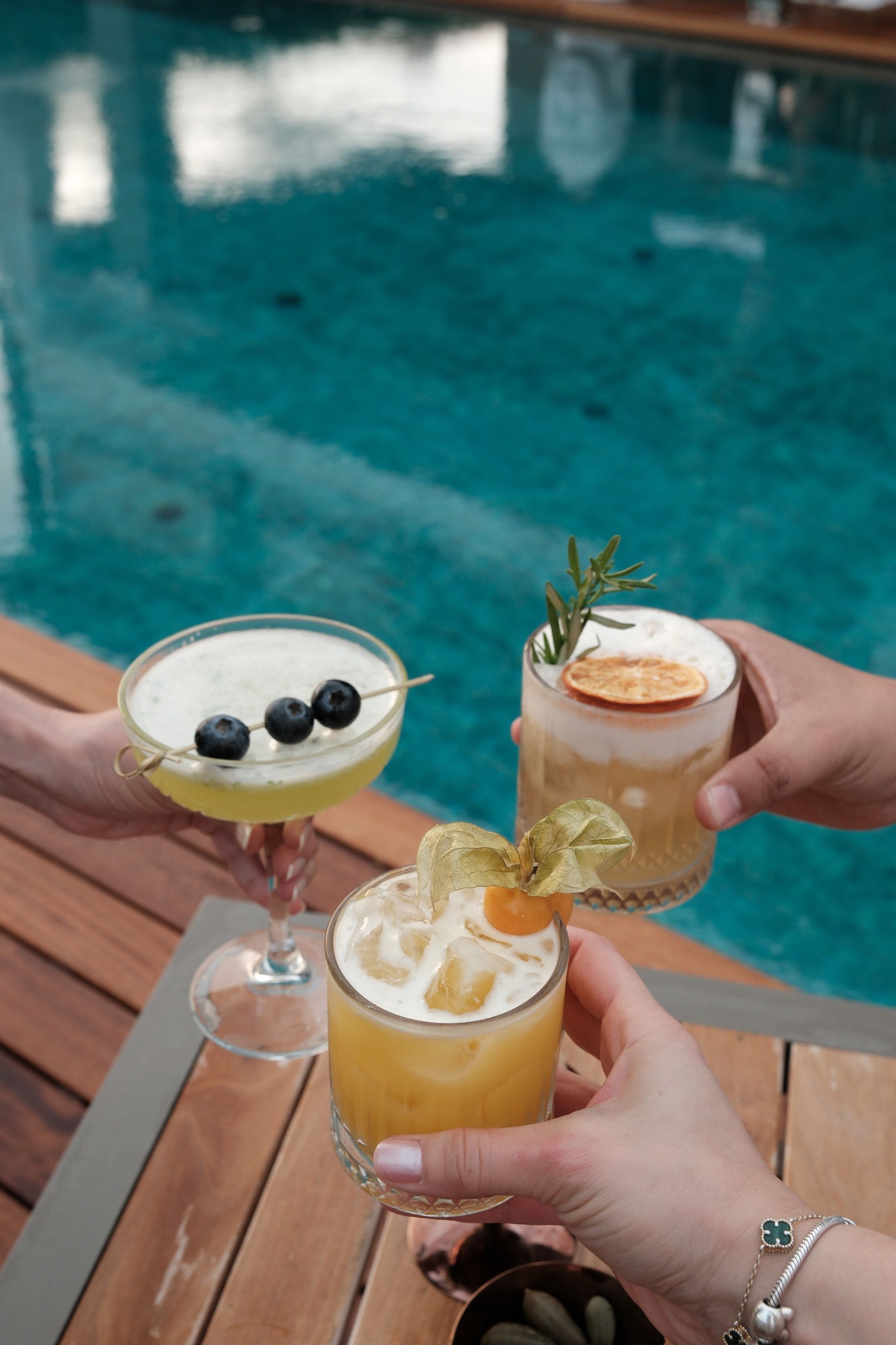 Two people holding cocktail glasses with a pool in the background.