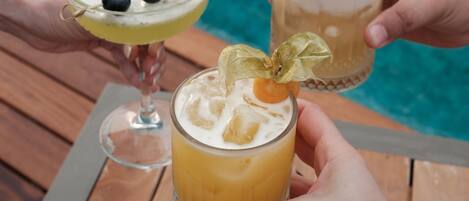 Two people holding cocktail glasses with a pool in the background.
