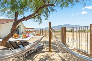 Una hamaca, sillones de descanso, una piscina y un área cercada con montañas al fondo.