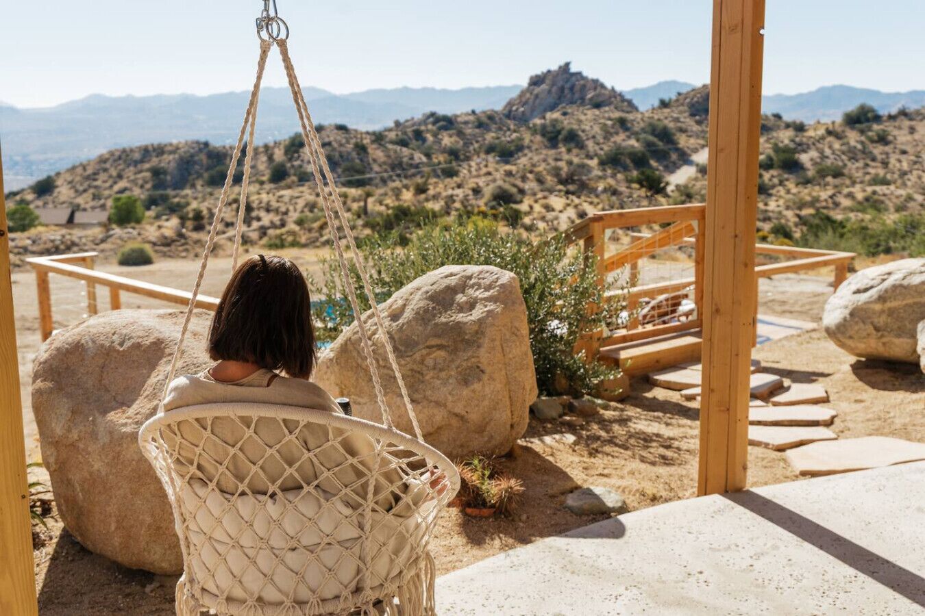 Una persona en una silla hamaca con vista a un paisaje desértico y montañas a lo lejos.