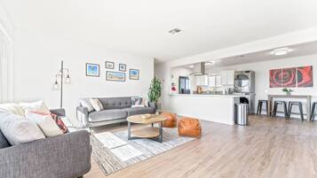 Ein modernes Wohnzimmer mit grauem Sofa, Couchtisch und Küchenbereich mit weißen Schränken und einer Edelstahl-Dunstabzugshaube.