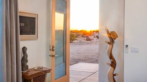 A room with a door leading outside, a framed picture on the wall, and a sculpture on a table. - Sun Gold | Secluded> Breathtaking Sunsets> Unique (Joshua Tree)