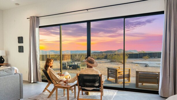 A room with a large sliding glass door, a sofa, and a table with chairs. - Sun Gold | Secluded> Breathtaking Sunsets> Unique (Joshua Tree)
