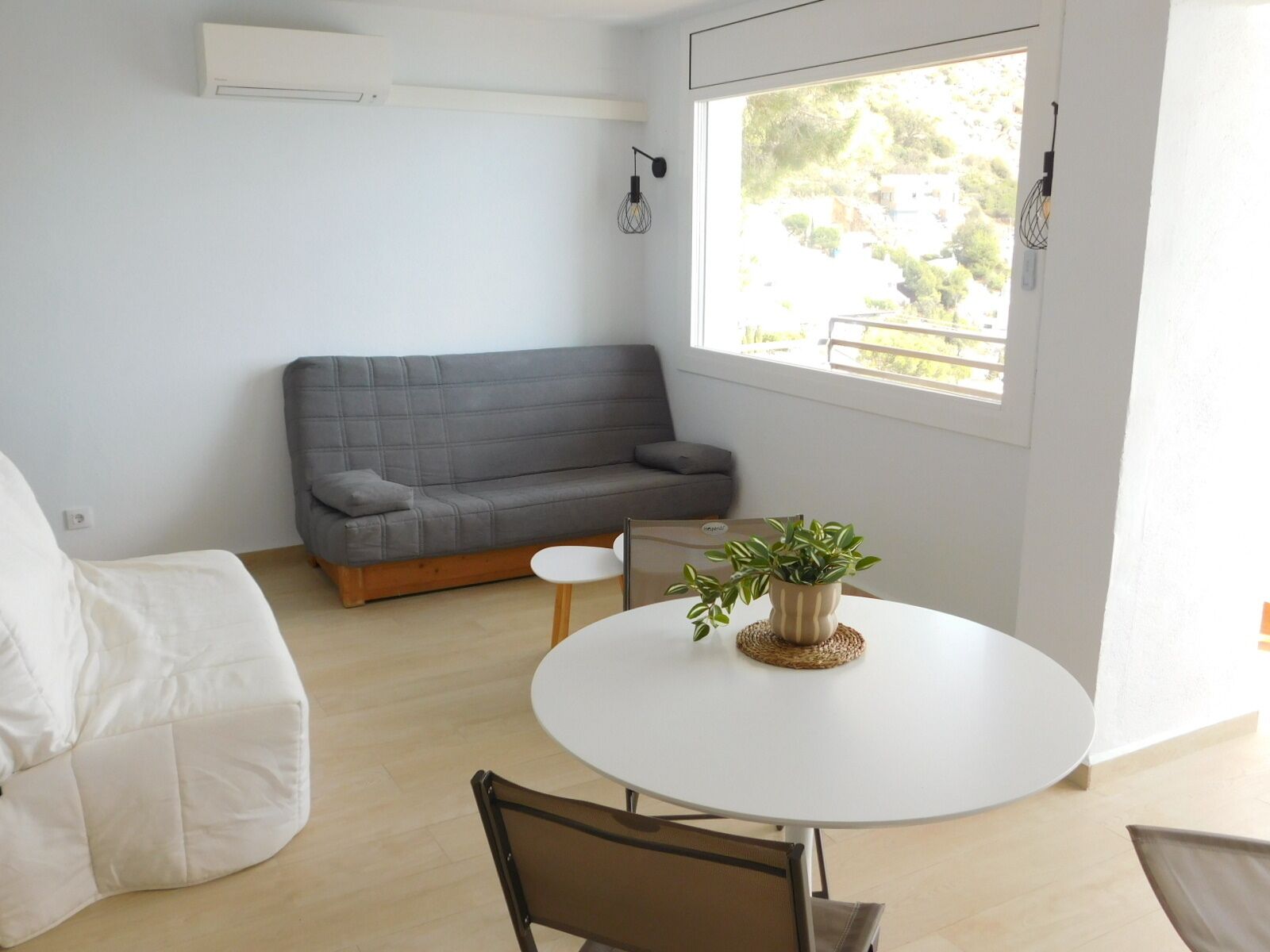 A modern living room with a grey sofa, a small white table with a plant, and a round white table.