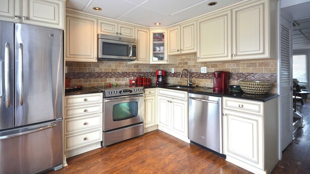 A modern kitchen with stainless steel appliances, white cabinetry, and a tiled backsplash.