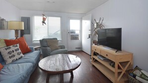 A living room with a blue sofa, a wooden coffee table, a television on a wooden stand, and a door with a window.