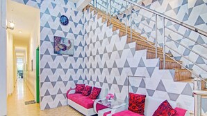 Een moderne woonkamer met een wand met een geometrisch patroon, een trap en twee banken met rode kussens.