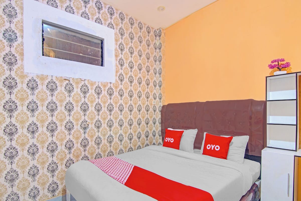 A bedroom with a bed, a window, patterned wallpaper, and a white wardrobe.
