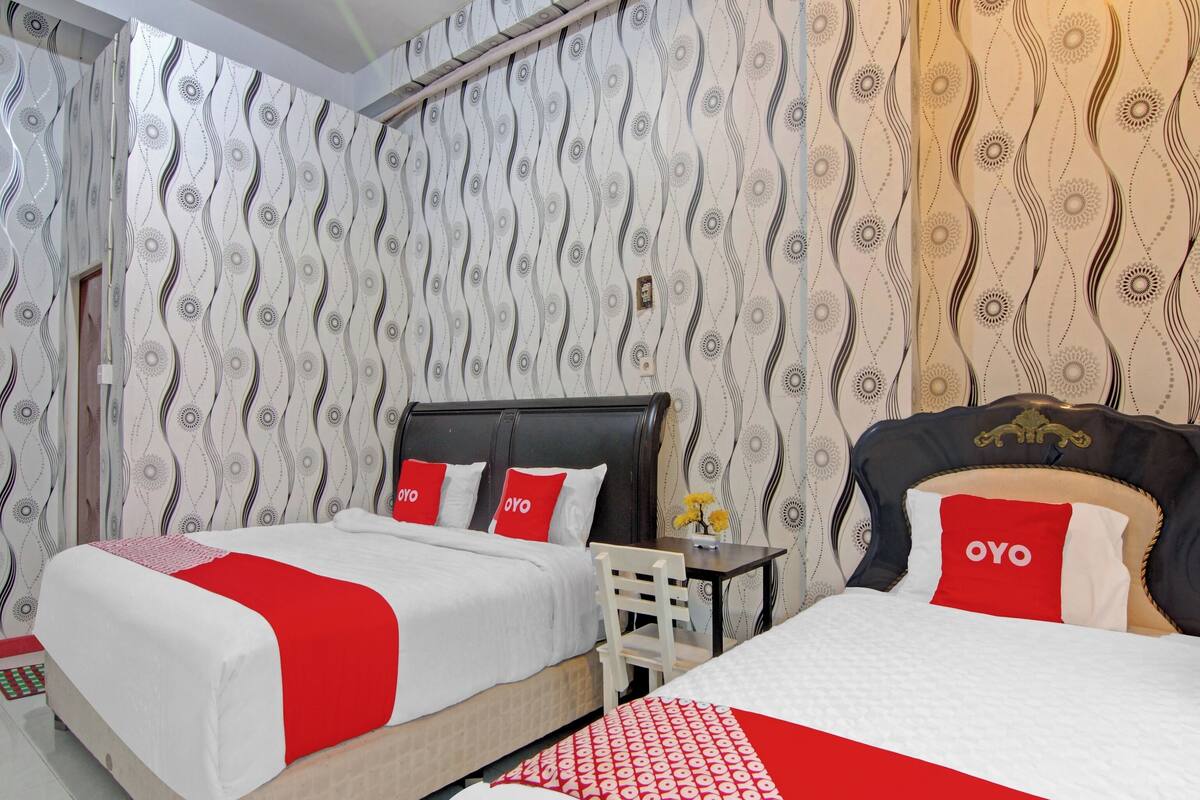A hotel room with two beds, each with red and white bedding, and a patterned wallpaper.