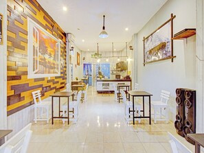 A restaurant with a modern interior, featuring a brick wall, white chairs, and a tiled floor. - OYO 90615 Jojo Homestay (Padang)