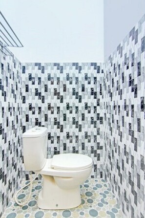 A bathroom with a toilet and a bidet, tiled walls, and a floor with circular patterns. - OYO 90615 Jojo Homestay (Padang)