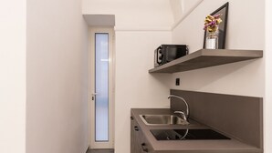 Una cocina compacta con un lavamanos integrado, un microondas y un estante pequeño con un florero.