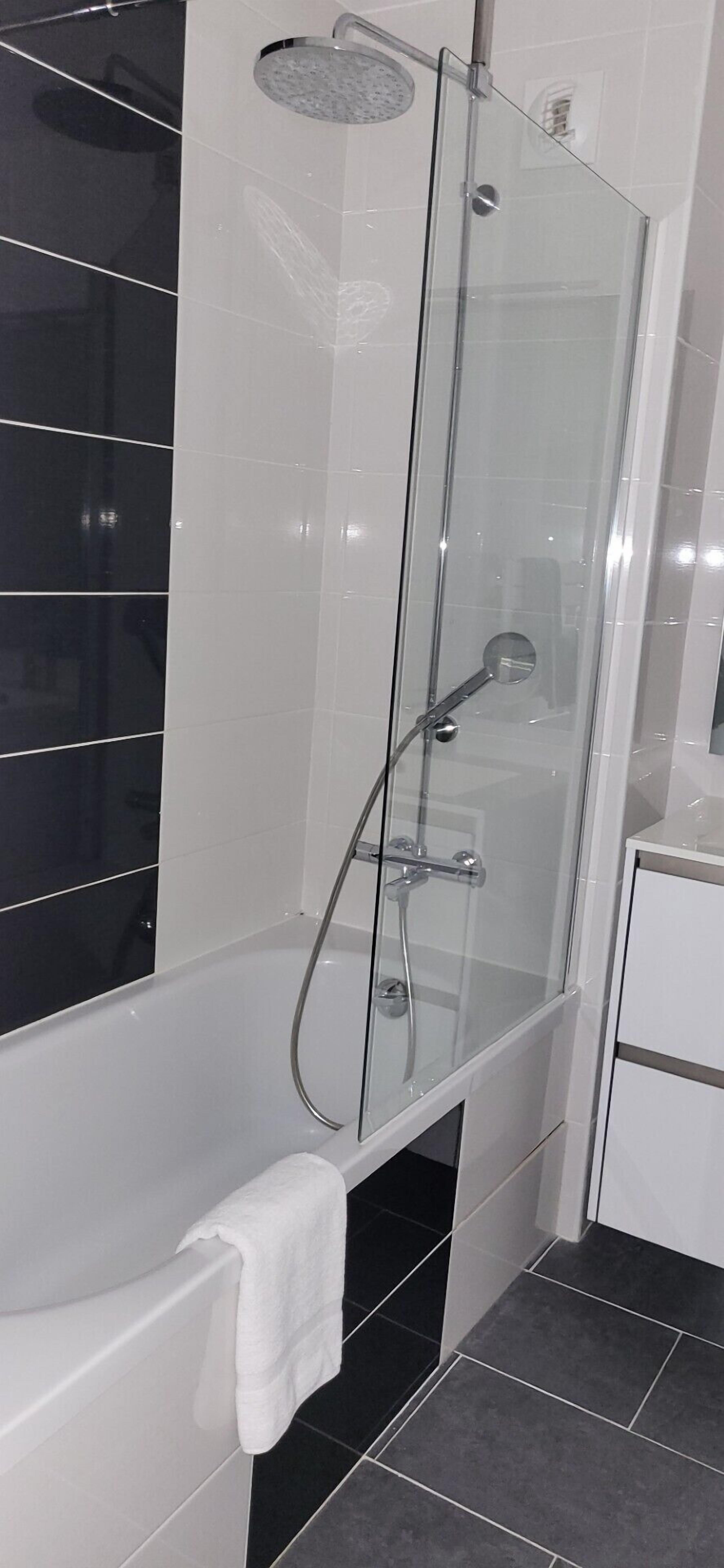 A modern bathroom with a glass-enclosed shower, a white bathtub, and black tiled flooring.