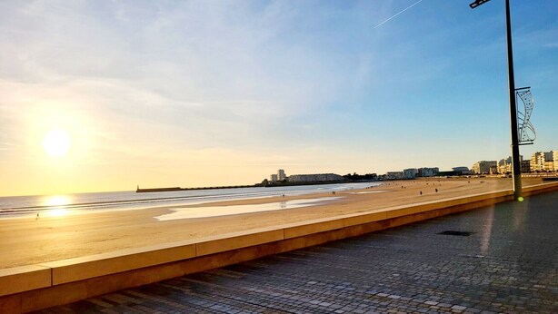 Une plage avec une promenade dallée et une structure métallique.