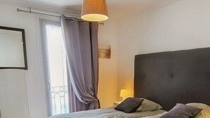 Une chambre à coucher avec un grand lit, un ventilateur de plafond, une fenêtre avec des rideaux et une table de chevet avec une lampe.