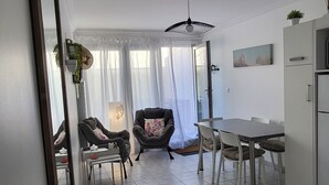 Une cuisine moderne avec des meubles blancs, un coin repas comprenant une table et des chaises, et une grande fenêtre agrémentée de rideaux légers.