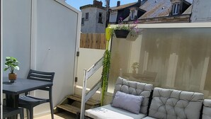 Une terrasse avec un canapé et des fauteuils, une petite table et une plante en pot.