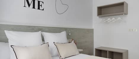 A neatly arranged bedroom with a bed, pillows, a wall-mounted shelf, and a bedside table.