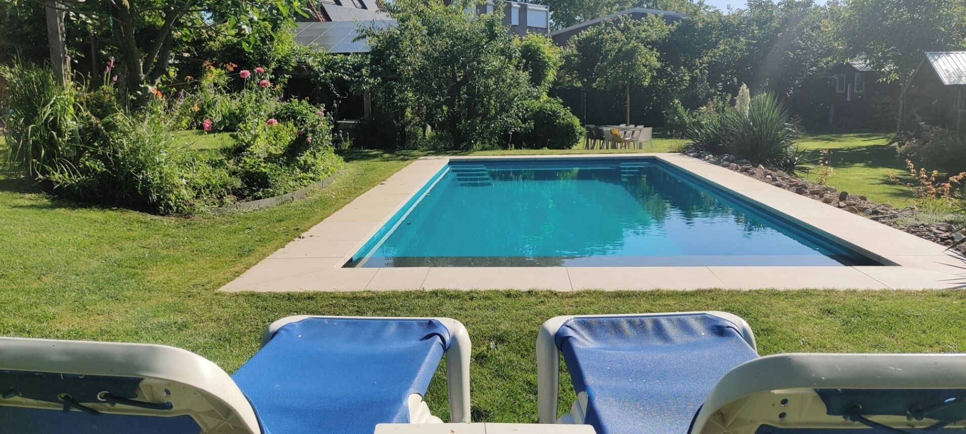 A rectangular swimming pool with two lounge chairs in the foreground.
