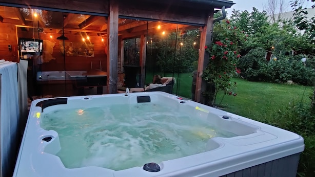 A hot tub in a covered outdoor area with wooden walls and string lights.