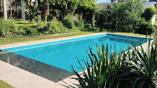 A rectangular swimming pool with clear blue water, surrounded by a well-maintained garden with various plants and flowers.