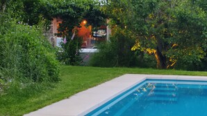 A swimming pool surrounded by lush greenery and a building with warm lighting in the background.