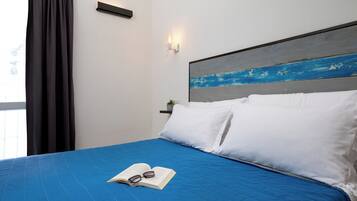 Un letto rifatto con una coperta blu, cuscini bianchi e un libro con gli occhiali sopra.