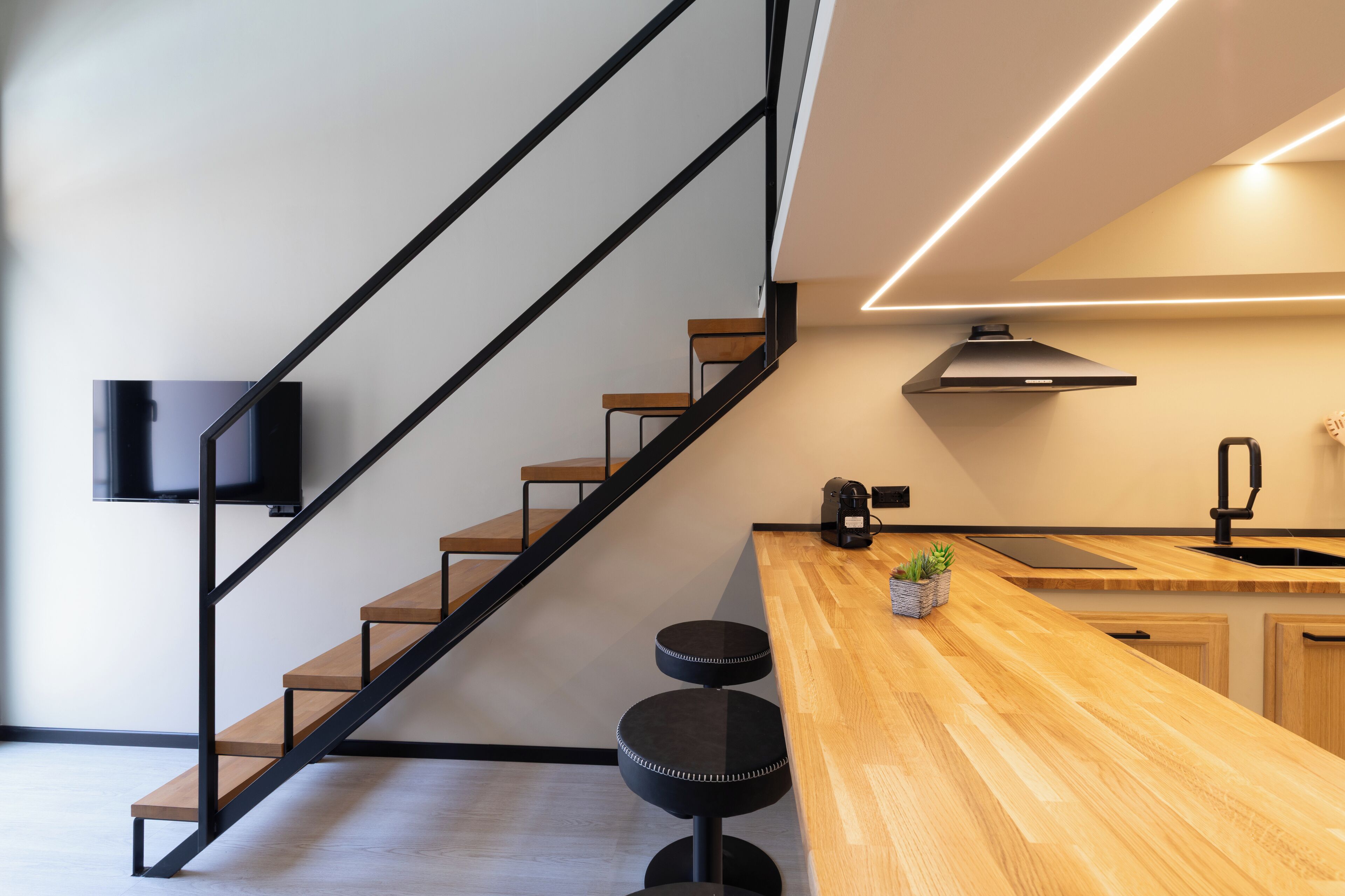 Una cocina moderna con encimera de madera, taburetes negros, estufa integrada y campana extractora negra.