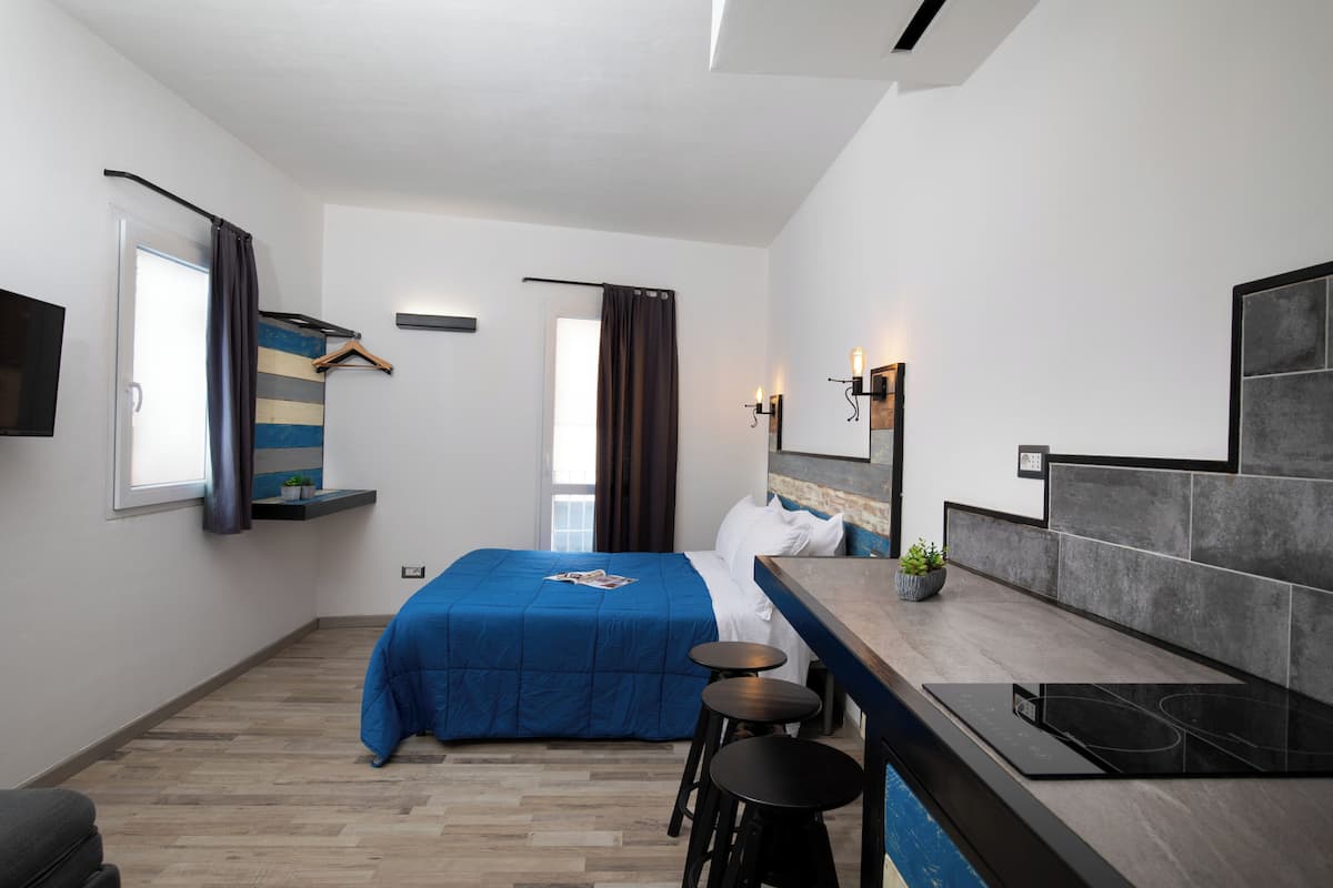 Ein kleines Hotelzimmer mit Bett, einer kompakten Küchenzeile und einer Sitzecke.