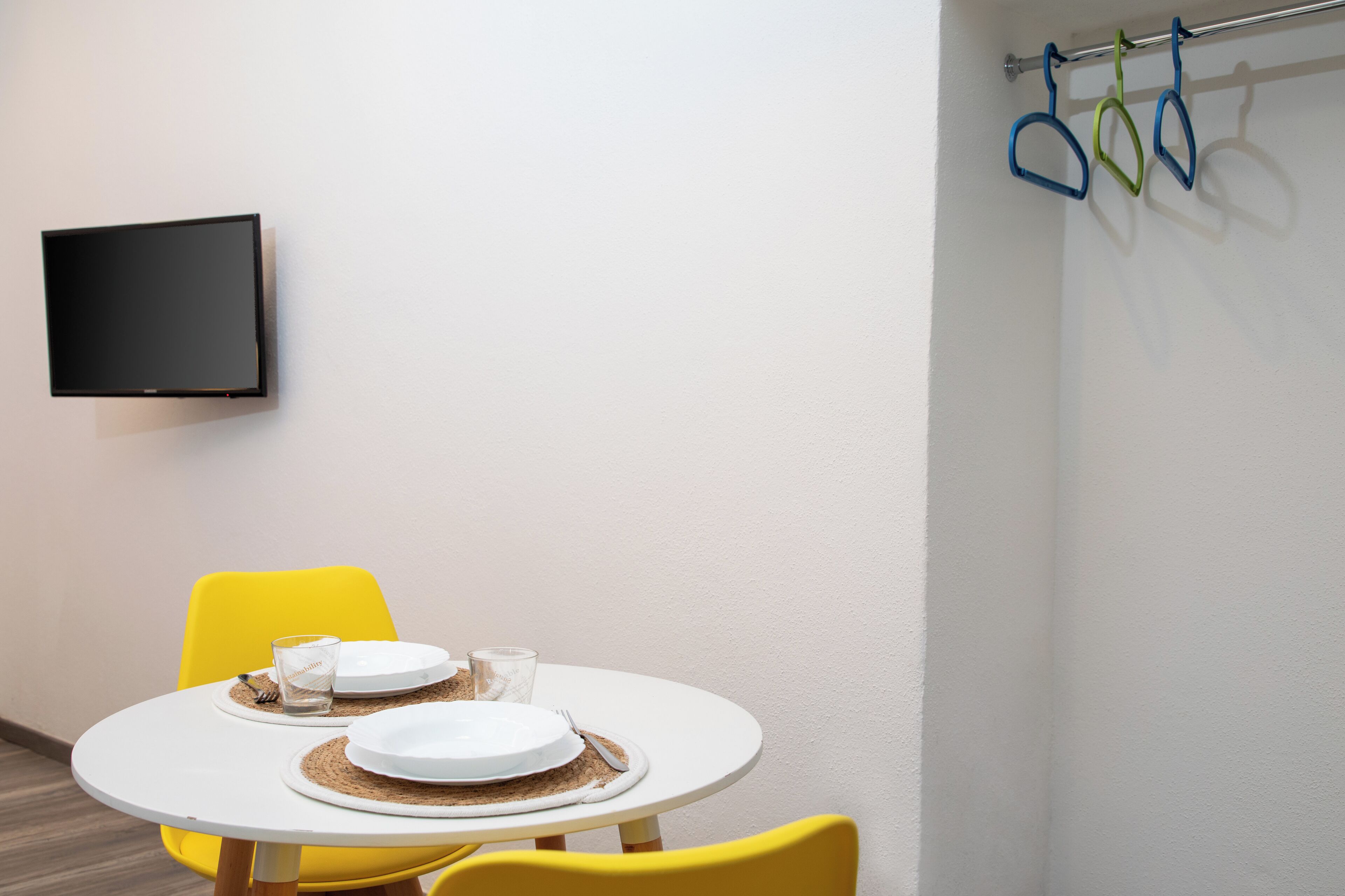 A dining area with a round table, yellow chairs, and a flat-screen TV mounted on the wall.
