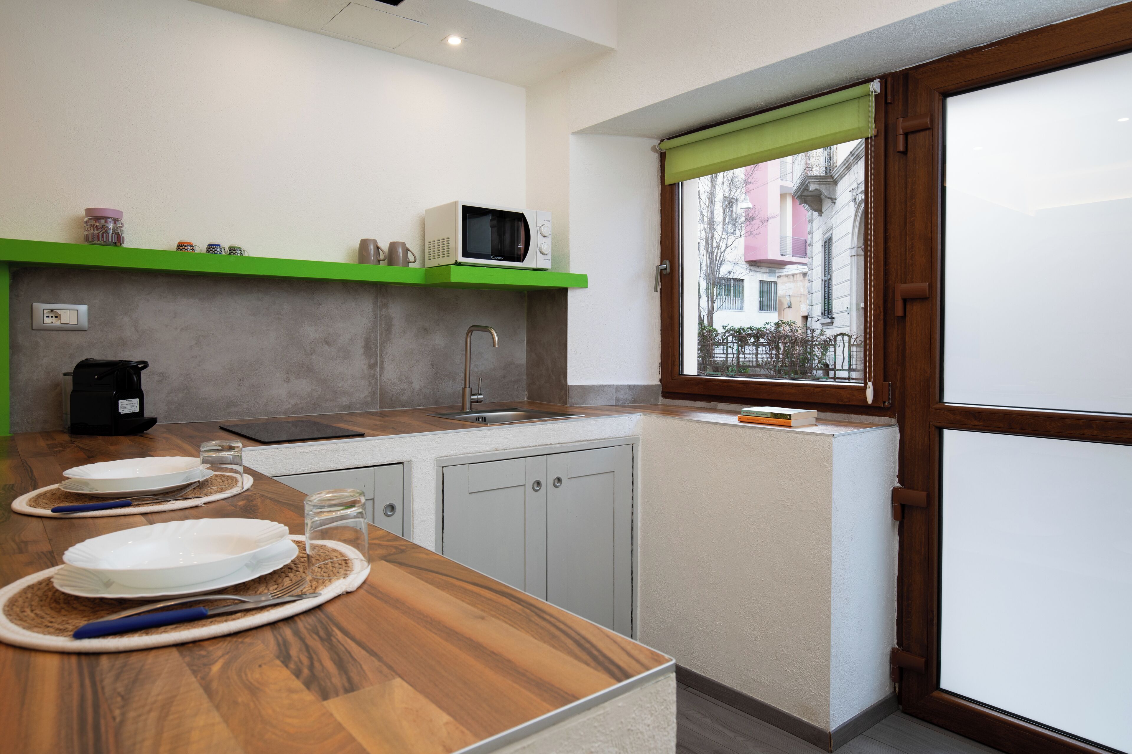 A modern kitchen with a wooden countertop, a built-in microwave, and a window with a view of the street.