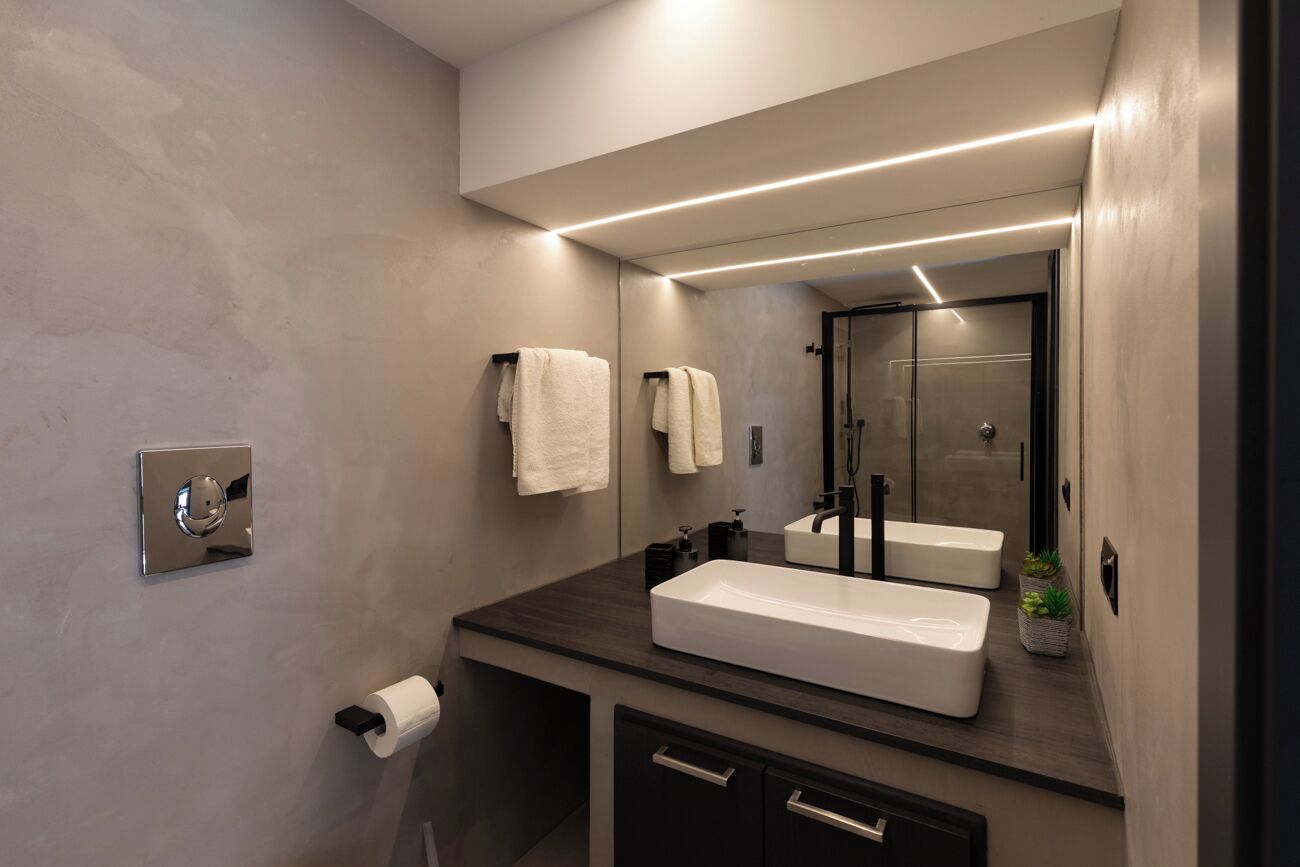 A modern bathroom with a large mirror, two sinks, a toilet, and a shower.