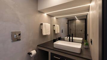 A modern bathroom with a large mirror, two sinks, a toilet, and a shower.