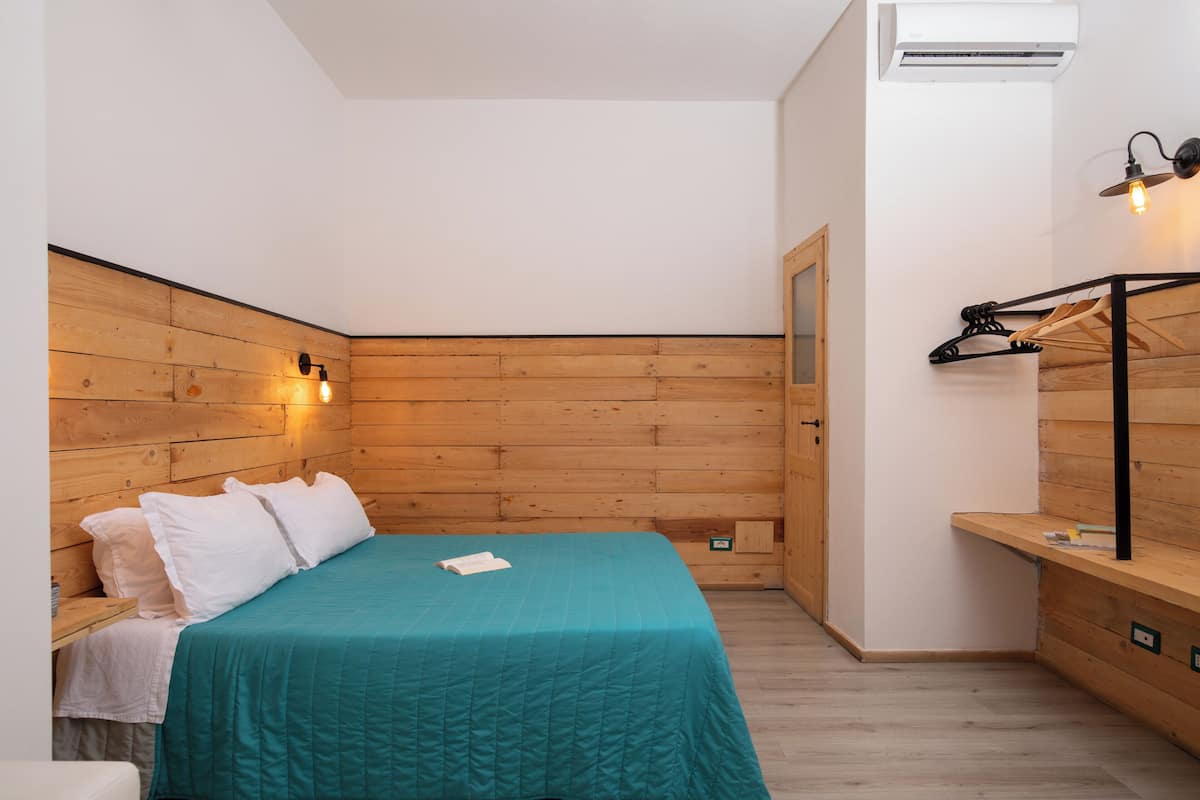 Ein kleines Schlafzimmer mit einem Holzkopfende, einer türkisblauen Bettdecke und einer Wandleuchte.