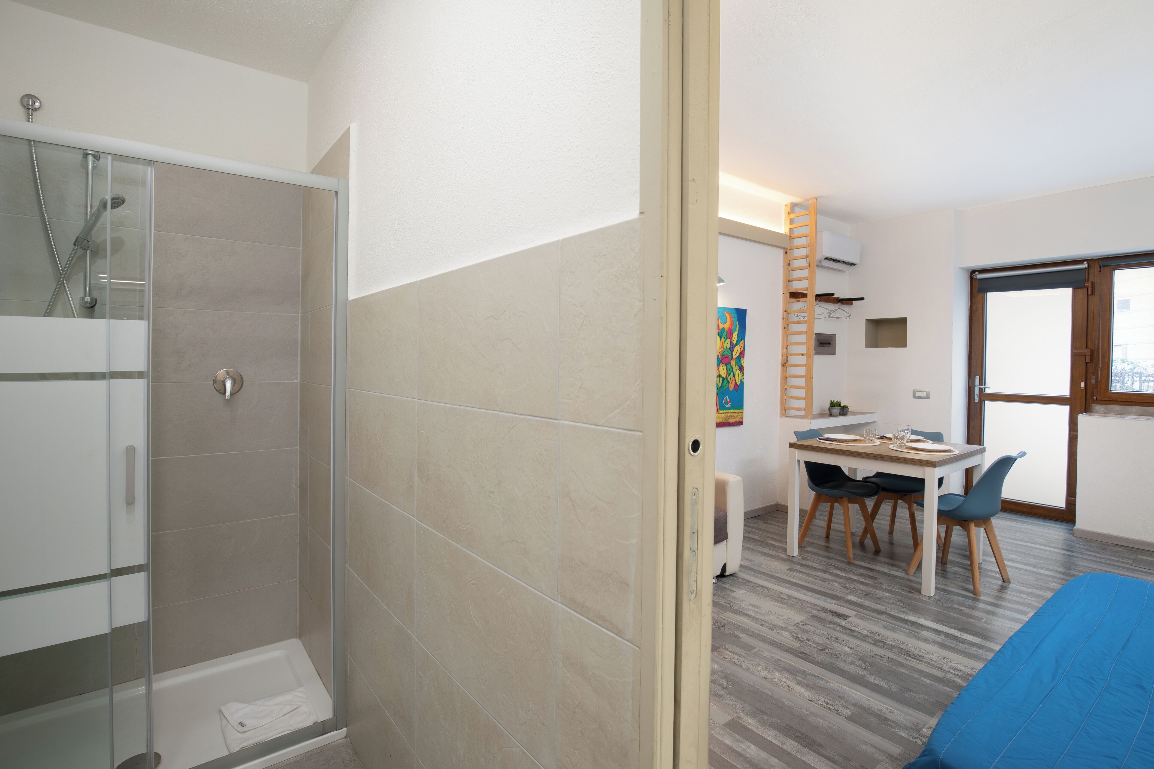 A modern bathroom with a glass shower enclosure, a white bathtub, and a wooden door.